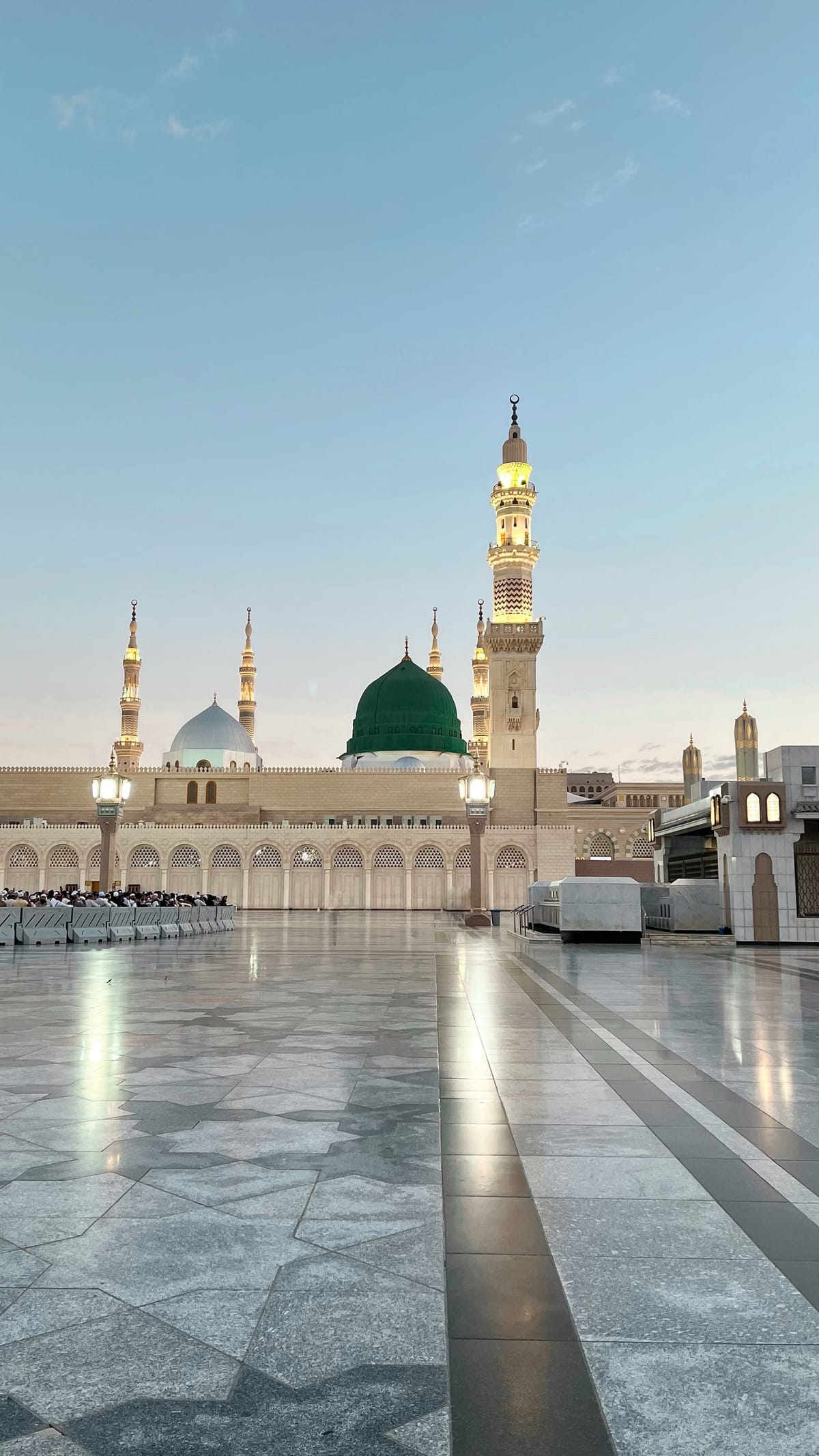 Al-Masjid an-Nabawi at dusk, its green dome and lit minarets above the polished marble of the courtyard