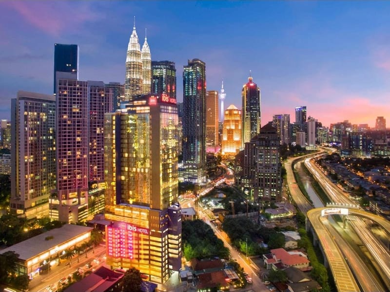 The ibis Kuala Lumpur City Centre lit at dusk with the Petronas Towers behind it
