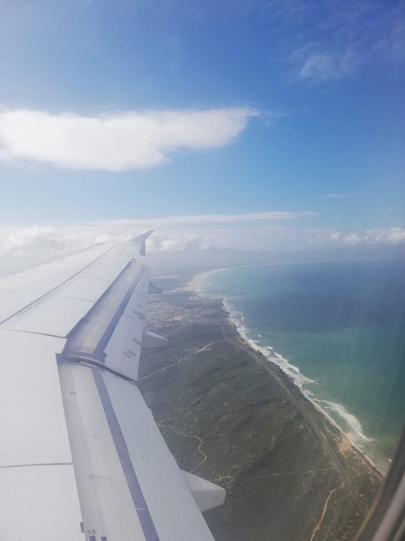 An aircraft wing above a coastline, the mountains dropping into the sea below